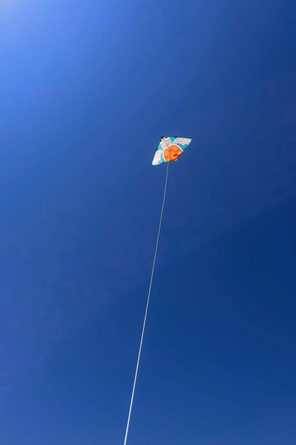 A small multicolored kite flies on a long white string against a deep blue sky.