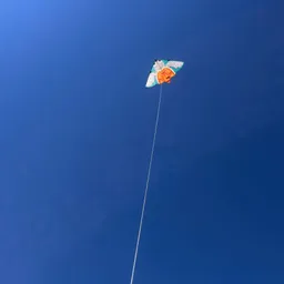 A small multicolored kite flies on a long white string against a deep blue sky.
