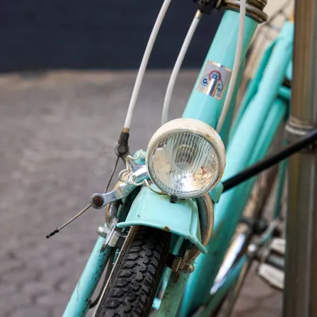 A weathered turquoise bicycle has a round headlamp above the front tire.